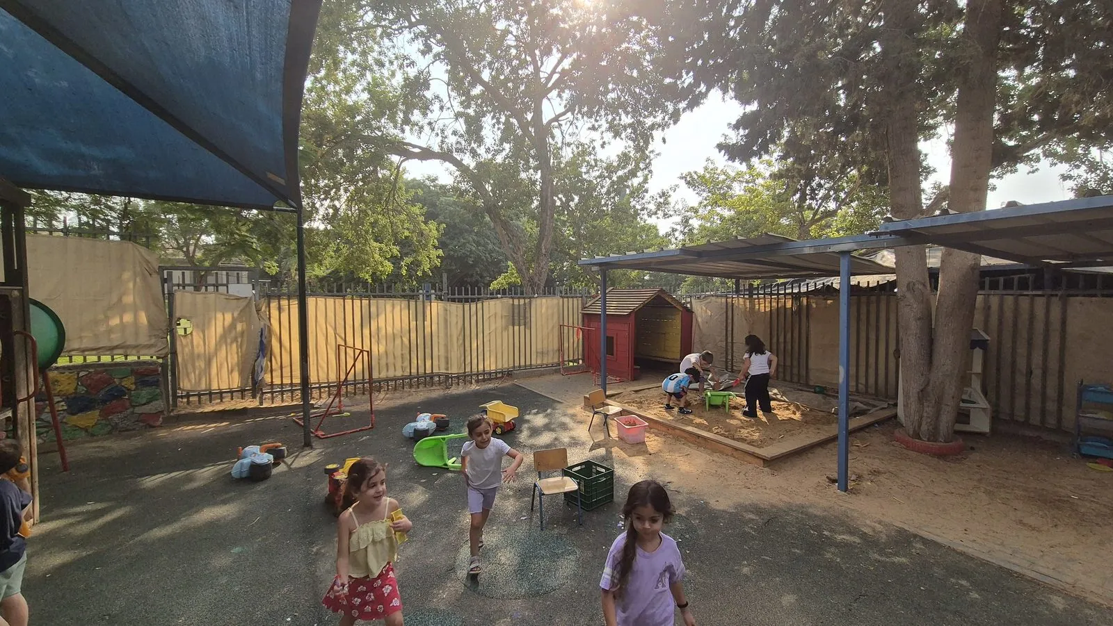 The old grey rubber surface next to the sandpit and playhouse, with children walking across the bare ground