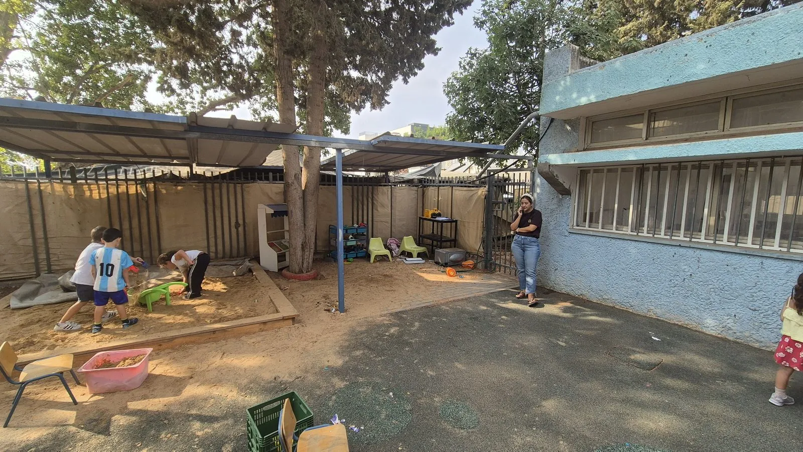 A corner of the original yard showing bare sand and plain grey surfacing beside the kindergarten building