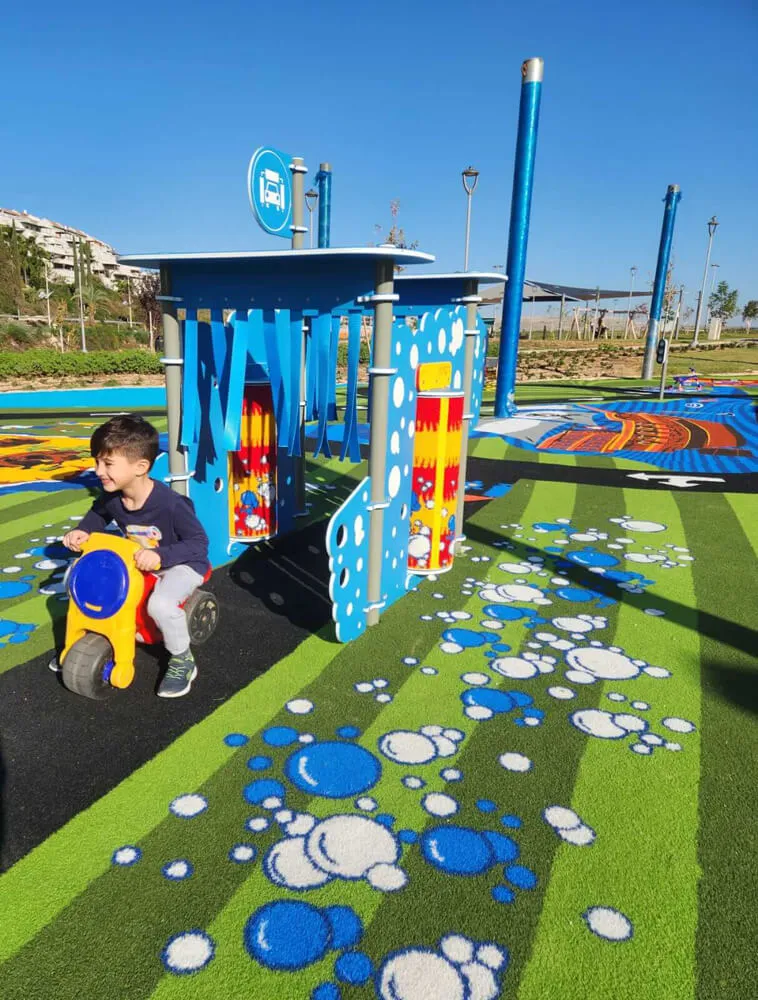 Toddler on a ride-on toy on a blue bubble-patterned play surface with a bus-stop prop